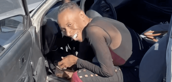 Person smiling while sitting in car doorway.